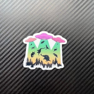 May include: A sticker with a colorful gradient background featuring three flying saucers and a group of dinosaurs. The saucers are pink, green, and blue. The dinosaurs are black silhouettes.