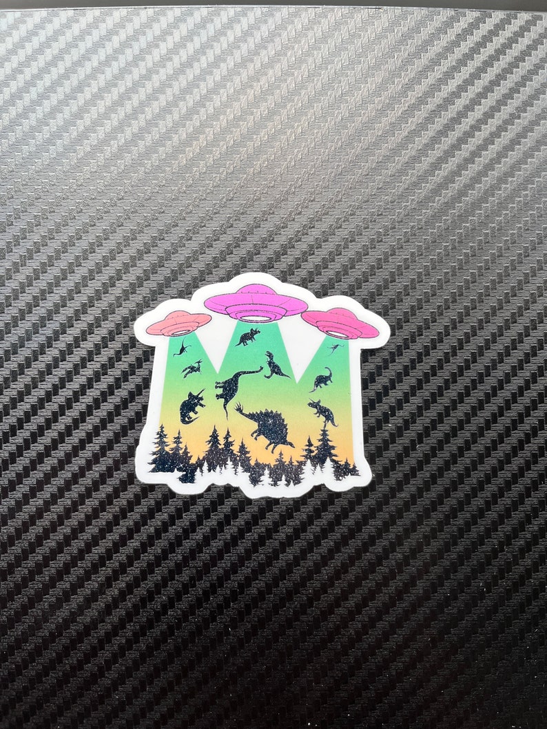 May include: A sticker with a colorful gradient background featuring three flying saucers and a group of dinosaurs. The saucers are pink, green, and blue. The dinosaurs are black silhouettes.
