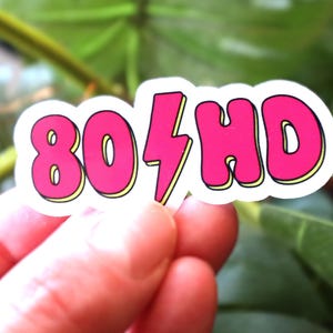 May include: A white sticker with pink lettering that says "80's HD" with a lightning bolt between the numbers and letters.