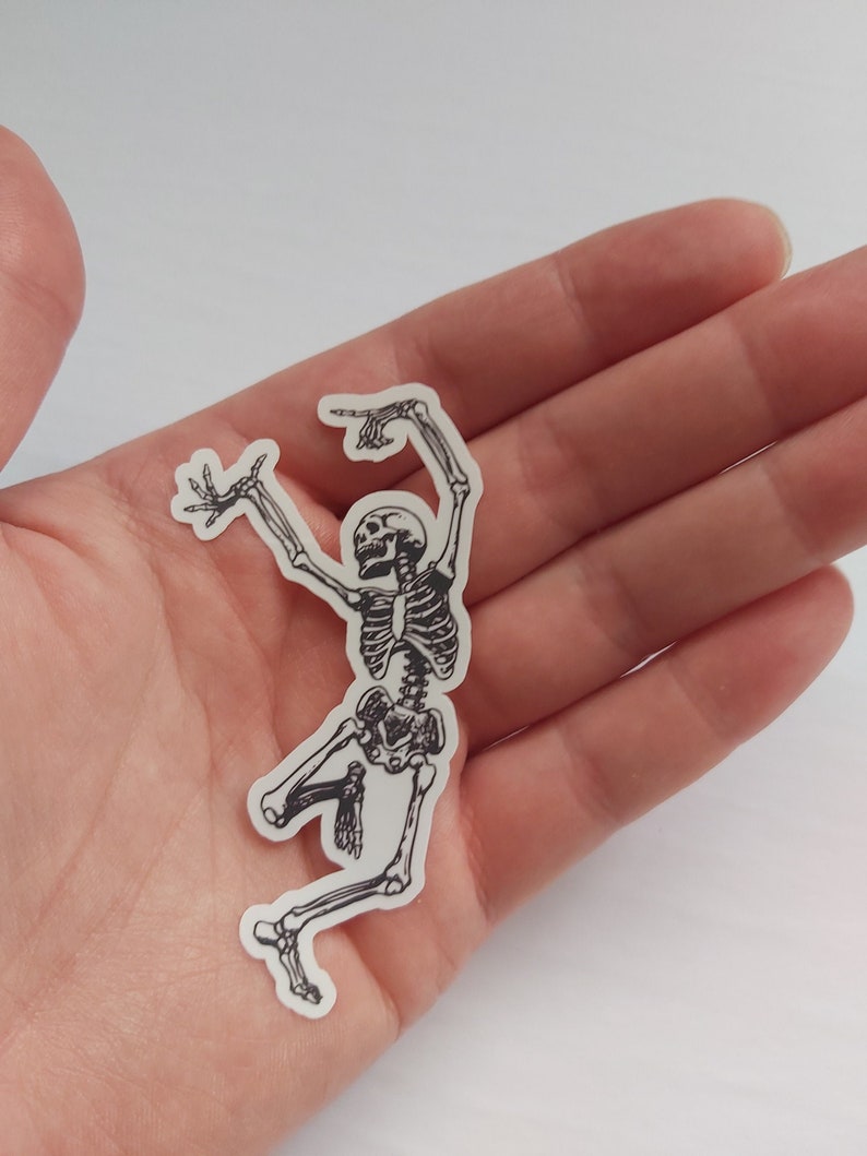 K&ouml;nnte beinhalten: Ein schwarz-wei&szlig;er Aufkleber eines tanzenden Skeletts mit erhobenen Armen.