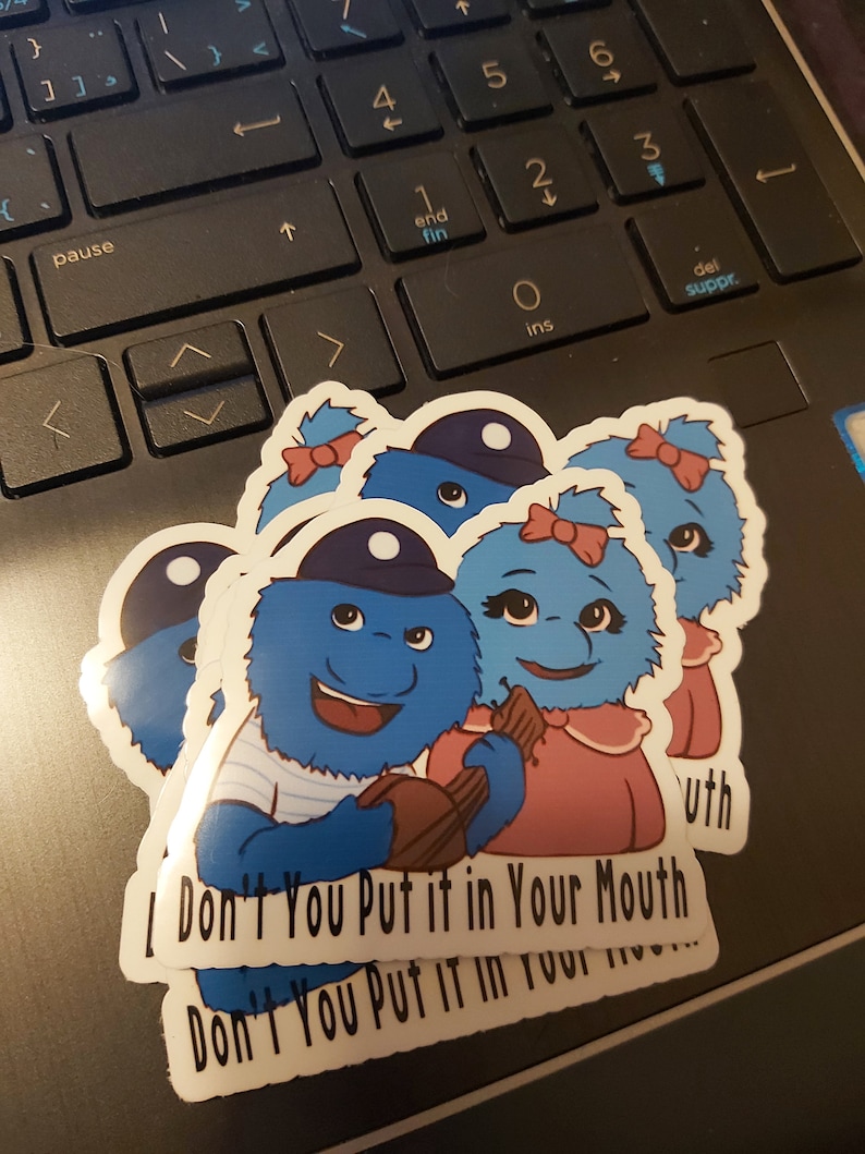 May include: Three blue fuzzy monster stickers with a white background. The stickers have a blue and white striped shirt, a pink dress, and a blue hat. The text on the stickers reads "I Don't You Put it in Your Mouth Don't You Put it in Your Mouth".
