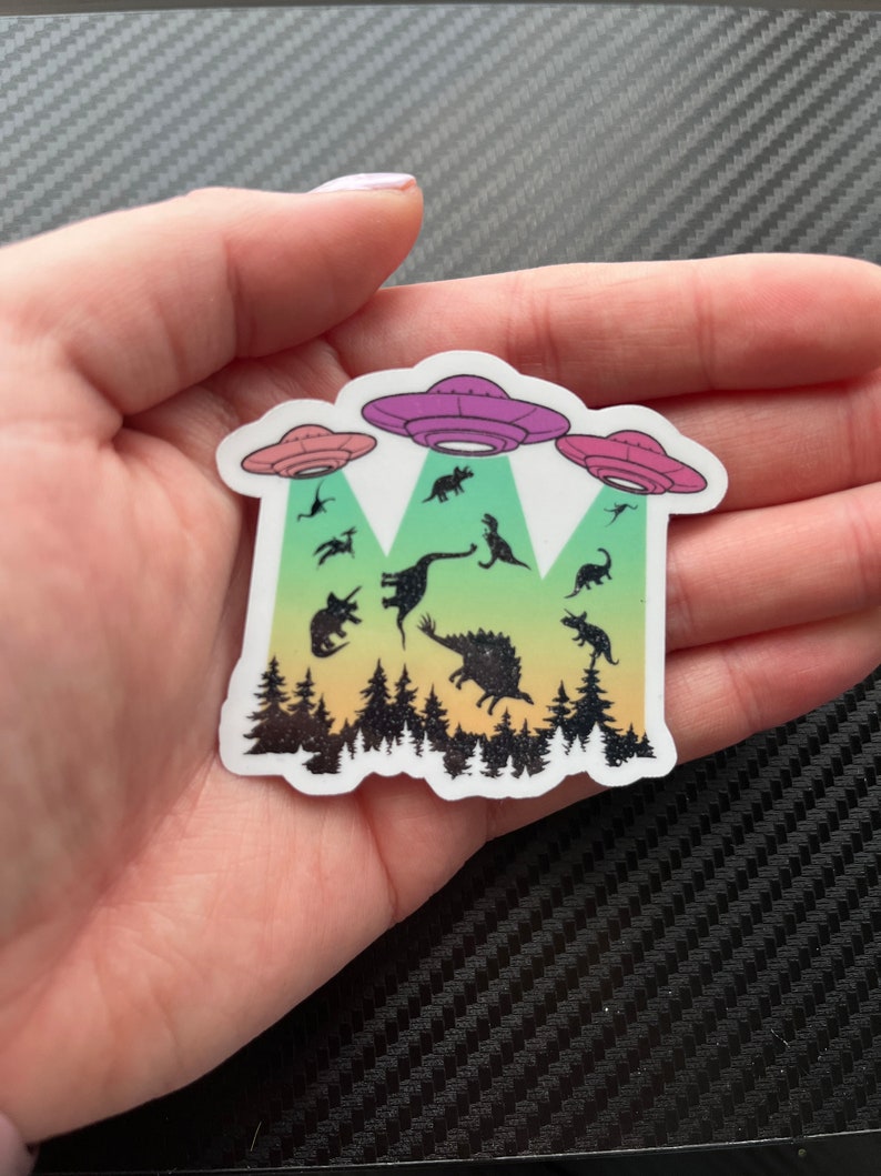 May include: A sticker with a rainbow gradient background featuring a group of dinosaurs being abducted by three flying saucers. The sticker is on a black and white carbon fiber background.