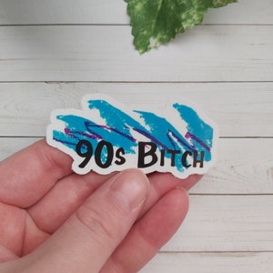 May include: A sticker with a blue and purple abstract design and the text "90s Bitch" in black.