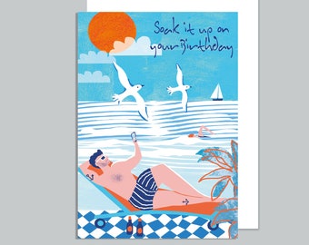 May include: A greeting card with a blue and white beach scene. A man is relaxing on a lounge chair with a drink. The text on the card reads "Soak it up on your birthday."