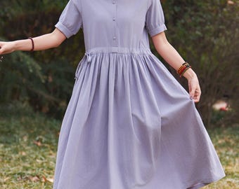 May include: A light purple dress with short sleeves and a collared neckline. The dress has a gathered waist and a flowing skirt. A straw hat with a checkered band and a small bow is worn. The person is standing in a grassy area.