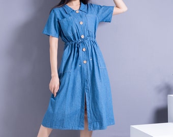 May include: A denim blue dress with short sleeves, a collared neckline, and wooden buttons. The dress features a drawstring waist and front pockets. A straw hat and white shoes complete the outfit.