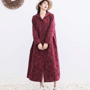May include: A long, burgundy hooded coat with a floral pattern. The coat has a button closure and a relaxed fit.