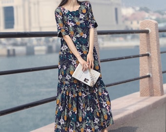 May include: A woman wearing a straw hat and a blue and white floral maxi dress with a ruffled hem. She is holding a book and standing on a bridge.