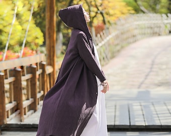 May include: A long, purple hooded cardigan with a textured pattern. The cardigan is worn over a white dress and the person is walking on a wooden bridge.