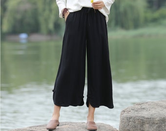 May include: A woman wearing a white top and black wide-leg pants with a drawstring waist. The pants have a loose, flowy fit and are made of a lightweight fabric.