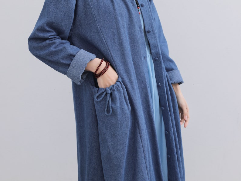 May include: A long-sleeved denim shirt dress with a button-up front and a drawstring pocket. The dress is a light blue colour.