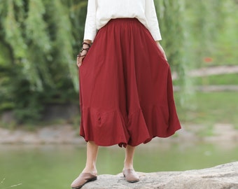 May include: A woman wearing a white top and a long, flowing burgundy skirt. The skirt has a ruffled hem and is made of a lightweight fabric.