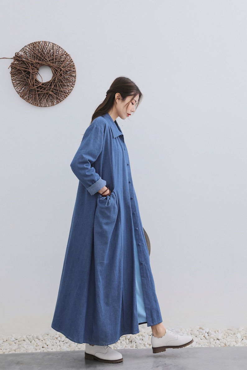 May include: A long, blue denim shirt dress with a collared neckline and button closure. The dress has a relaxed fit and features a single patch pocket on the left side.