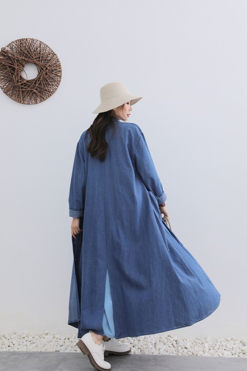 May include: A long, blue denim dress with a split up the back. The dress has long sleeves and a relaxed fit. The model is wearing a straw hat and white shoes.