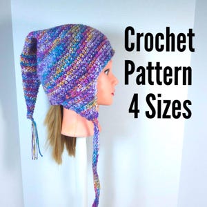 Może przedstawiać: Kolorowa czapka szydełkowa z długim, spiczastym końcem i nausznikami jest prezentowana na głowie manekina. Czapka wykonana jest z przędzy w odcieniach fioletu, niebieskiego, żółtego i różowego. Widoczny jest tekst "Crochet Pattern 4 Sizes".