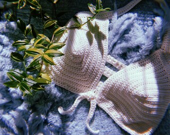 May include: White crochet halter top with a tie closure. The top is laid out on a blue fuzzy surface.
