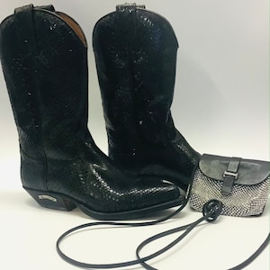 May include: A pair of black cowboy boots with a matching small purse. The boots have a textured pattern and a pointed toe. The purse has a silver chain and a buckle closure. The items are on a white background.
