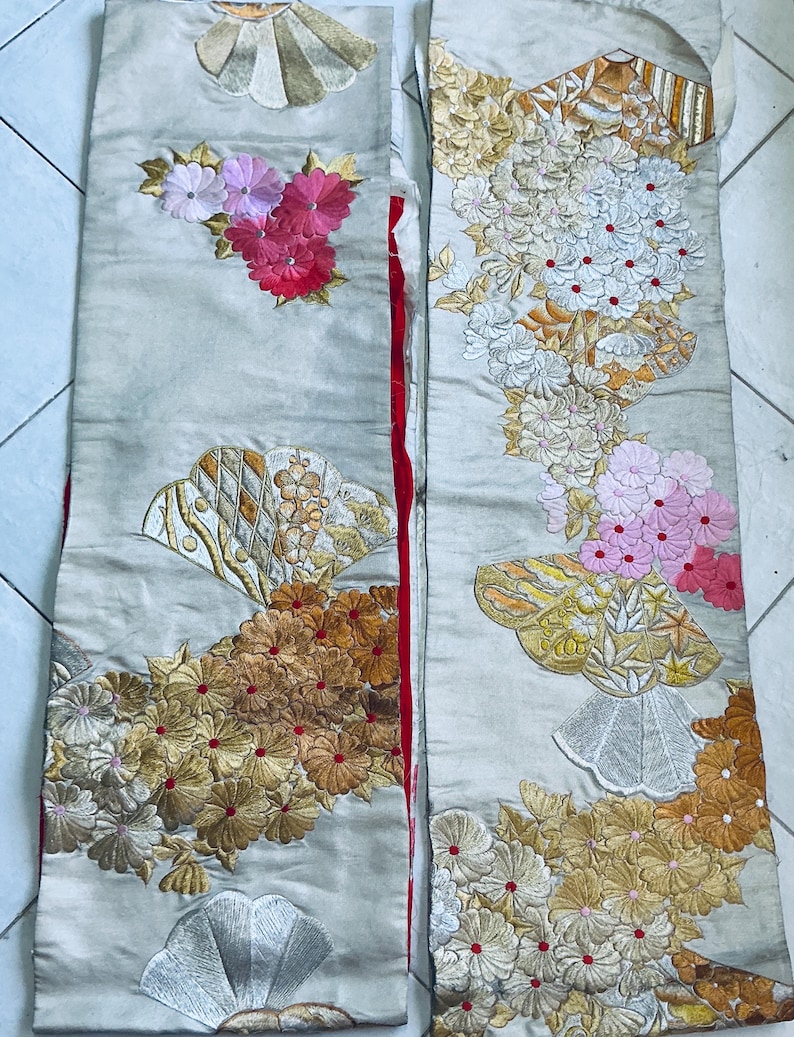 Op de afbeelding: Twee cr&egrave;mekleurige, geborduurde stoffen panelen. E&eacute;n paneel heeft een cluster van roze en rode bloemen, de andere heeft bloemen in wit, goud en roze. Beide panelen hebben waaiervormige ontwerpen. Waarschijnlijk onderdeel van een kledingstuk.