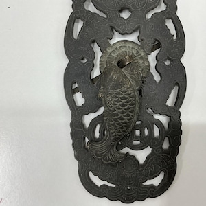 May include: Ornate, dark metal door pulls with a fish-shaped handle. The pulls have a decorative, openwork design with floral and geometric patterns. The fish handle is detailed with scales and fins.