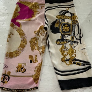 Könnte beinhalten: Eine Hose aus rosa und weißer Seide mit schwarzem und weißem Besatz. Die Hose hat ein florales und reiterliches Design mit goldenen Akzenten. Die Hose ist aus einem weichen, fließenden Stoff gefertigt.