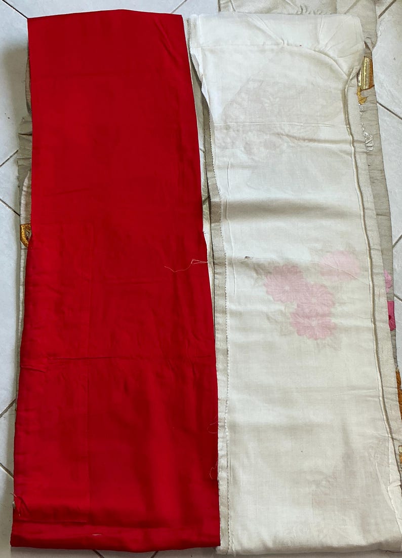 Op de afbeelding: Een felrood stoffen paneel naast een wit stoffen paneel met roze bloempatronen. Het witte paneel heeft een decoratieve rand met gouden accenten. De stoffen liggen op een lichtgekleurd oppervlak.