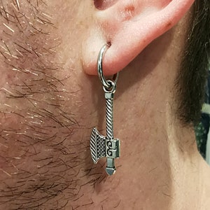 May include: Silver axe earring with a hoop and a twisted chain. The axe has a detailed design and a small inscription.
