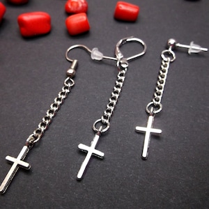 Può includere: Orecchini a croce color argento con dettagli a catena. Gli orecchini presentano tre stili diversi: un pendente lungo, un gancio e un perno. Le croci sono piccole e semplici, con una finitura lucida. Pietre rosse sono sparse sullo sfondo.