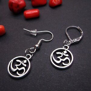 May include: A pair of silver earrings with a circular pendant featuring the Om symbol. The earrings have a hook fastening.