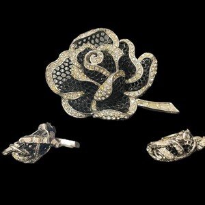 May include: A black and silver rose brooch with rhinestones. The rose is made of a textured material and has a delicate stem.