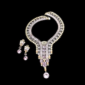 May include: A vintage rhinestone necklace and earrings set. The necklace features a large, teardrop-shaped pendant with a cascading design of clear and pink rhinestones. The earrings are simple and elegant, with a single, round rhinestone.