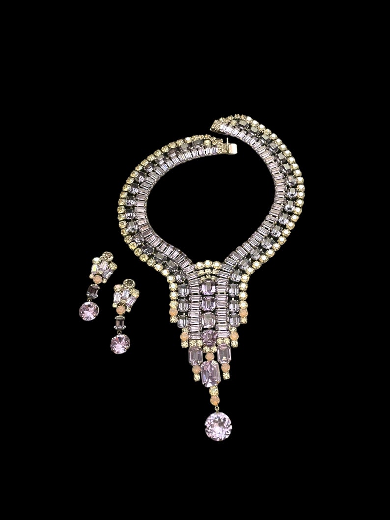 May include: A vintage rhinestone necklace and earrings set. The necklace features a cascading design with clear and pink rhinestones. The earrings are teardrop shaped with a single pink rhinestone.
