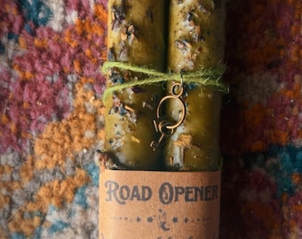 Puede incluir: Dos velas cónicas de color verde oliva atadas con un cordel verde y un pequeño dije de llave de bronce. Las velas están incrustadas con hierbas secas y envueltas en una etiqueta de papel color canela que dice ROAD OPENER, Overcome life obstacles and open paths.