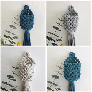 May include: Four macrame plant hangers in different colours. Two are a light grey colour and two are a teal blue colour. The hangers are made with a thick rope and have a tassel at the bottom.