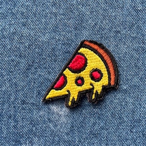 May include: A yellow and red embroidered pizza slice patch with a black outline. The patch is on a blue denim background.