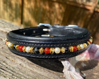 Op de afbeelding: Zwarte leren hondenhalsband met een decoratieve kralenrand. De rand is versierd met rode, witte, gouden en zwarte kralen.