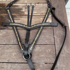 May include: A dark brown leather horse breastplate featuring a curved browband and two side straps adorned with a row of multi-colored translucent beads in shades of yellow, orange, and clear. The harness includes silver-toned metal rings and buckles.