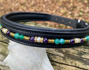 Può includere: Collare per cavallo in pelle nera con un bordo decorativo di perline verdi, viola e bianche. Le perline sono intervallate da accenti dorati.