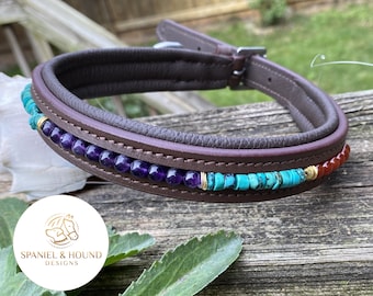 May include: A brown leather dog collar with a decorative trim of amethyst, turquoise, and carnelian beads. The collar has a silver buckle and is accented with gold accents.