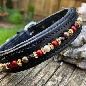 Puede incluir: Collar de perro de cuero negro con un borde decorativo de cuentas rojas, doradas, blancas y marrones.