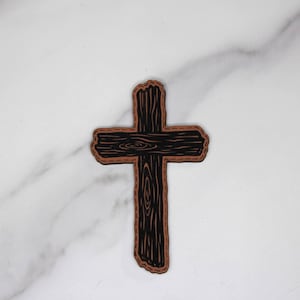 May include: A wooden cross with a dark brown grain pattern and a lighter brown border. The cross is a symbol of faith and spirituality, and is often used in religious contexts. The cross is made of wood and has a rustic, handmade appearance.