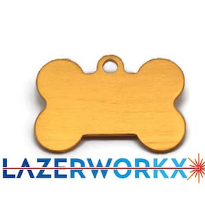 May include: A gold-coloured metal pet ID tag shaped like a bone with a small circular hole at the top for attachment. Below the tag, the text LAZERWORKX is printed in blue capital letters with a red laser graphic extending through the letters.