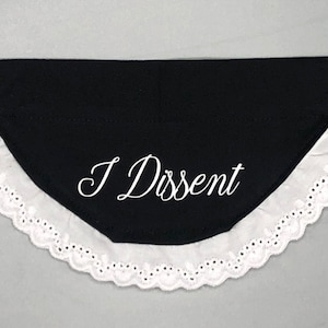 May include: Black dog bandana with white lace trim and the text "I Dissent" embroidered in white.