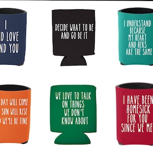 May include: Six different colorful can coolers with various sayings printed on them. The sayings include: "I and love and you", "Decide what to be and go be it", "I understand because my heart and hers are the same", "The day will come the sun will rise and we'll be fine", "We love to talk on things we don't know about", and "I have been homesick for you since we met".