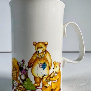 May include: White ceramic mug with a cartoon illustration of three teddy bears. The bears are depicted in a cartoon style, with one holding a flower and another with a patch on its belly. The mug has a curved handle.
