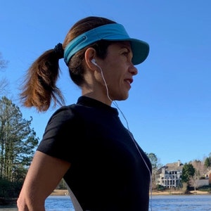 May include: A woman wearing a black shirt and a blue visor with a ponytail. She is wearing white earbuds and looking to the right.
