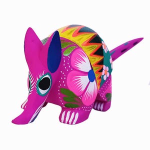 Peut inclure: Figurine d'armadillo en bois peint à la main. Le corps rose vif est orné de motifs floraux et géométriques roses, blancs, jaunes, verts et bleus. L'armadillo a un long museau et une queue, et est une pièce unique d'art populaire.