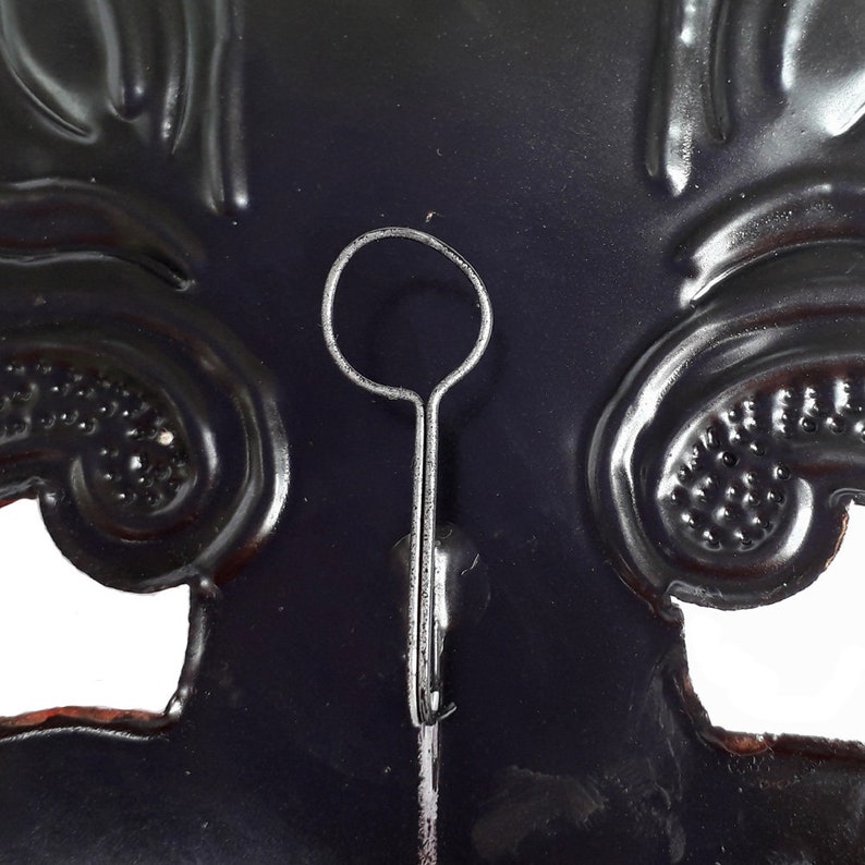 Puede incluir: Una m&aacute;scara de metal negro con un dise&ntilde;o decorativo. La m&aacute;scara tiene un lazo de metal en la parte superior para colgar.