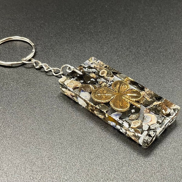 Porte clé en résine avec chaîne en métal plaquée argent et insertion de petites pierres d’obsidienne et breloque trèfle à quatre feuilles.