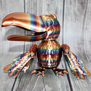 May include: A colorful toucan figurine with iridescent paint, featuring a large beak and detailed wings. The figurine is made of a metallic material and has a textured surface.