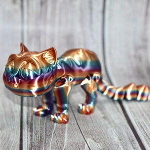 May include: A rainbow-colored cat figurine with a playful expression. The figurine is made of a shiny, metallic material and has a long, curled tail.
